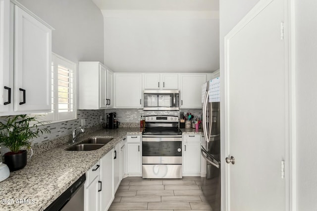 kitchen with white cabinets, decorative backsplash, light stone counters, appliances with stainless steel finishes, and a sink