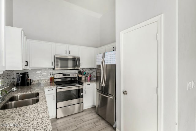 kitchen with a sink, white cabinets, appliances with stainless steel finishes, decorative backsplash, and wood tiled floor