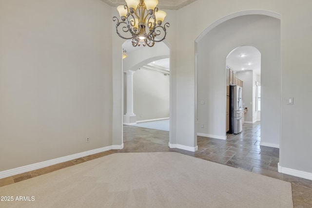 unfurnished dining area with arched walkways, baseboards, stone tile flooring, and a notable chandelier