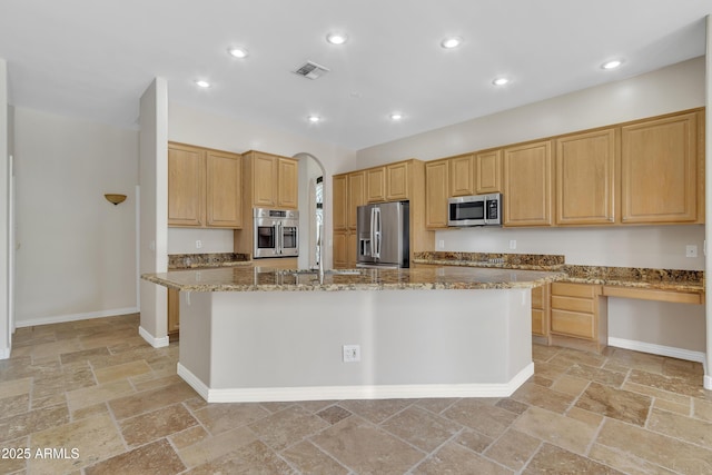 kitchen with visible vents, appliances with stainless steel finishes, light stone countertops, stone tile floors, and an island with sink
