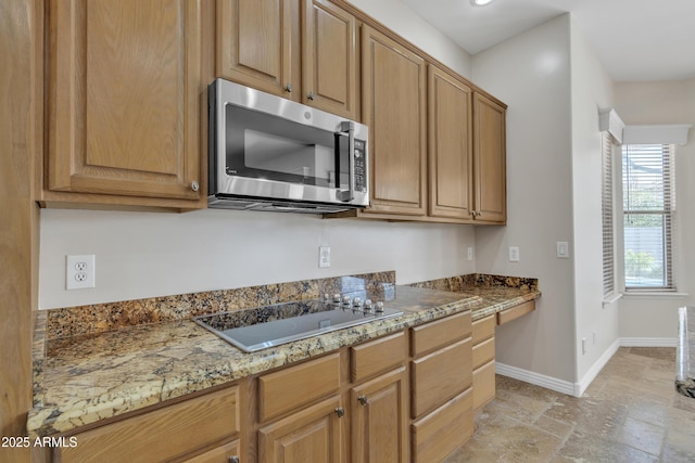 kitchen with stone tile floors, light stone countertops, baseboards, black electric stovetop, and stainless steel microwave