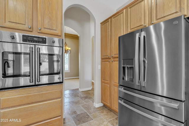kitchen with arched walkways, a chandelier, stainless steel appliances, baseboards, and stone tile flooring