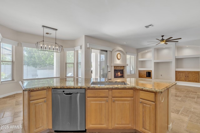 kitchen featuring a warm lit fireplace, a sink, stainless steel dishwasher, visible vents, and stone tile flooring