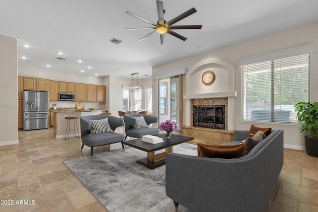 living area with ceiling fan, visible vents, stone tile floors, baseboards, and a premium fireplace