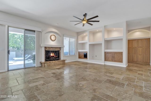 unfurnished living room with stone tile flooring, built in features, a fireplace, a ceiling fan, and a wealth of natural light