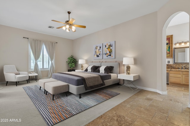 bedroom with visible vents, stone tile floors, baseboards, ensuite bathroom, and arched walkways