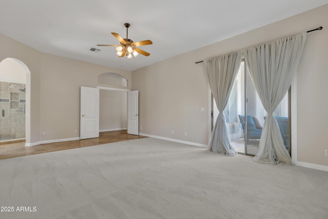 carpeted empty room with arched walkways, baseboards, a ceiling fan, and visible vents