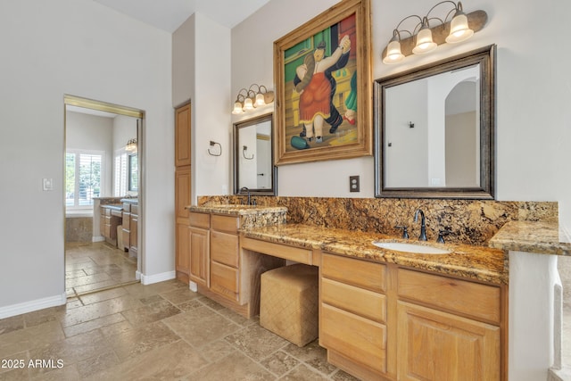 bathroom featuring stone tile floors, double vanity, baseboards, and a sink