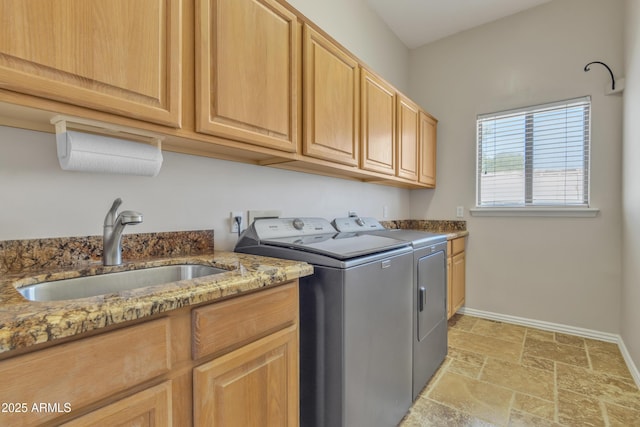 clothes washing area with cabinet space, a sink, stone tile floors, baseboards, and washing machine and dryer