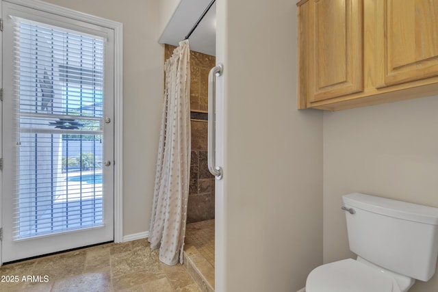 bathroom featuring baseboards, toilet, and tiled shower