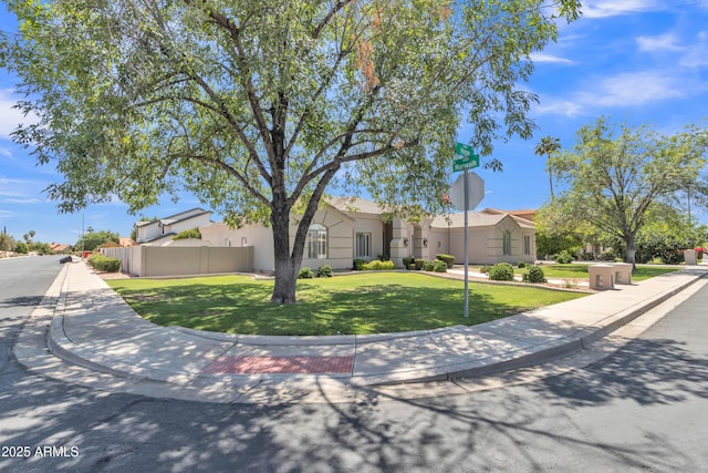 view of front of house featuring fence, stucco siding, and a front yard