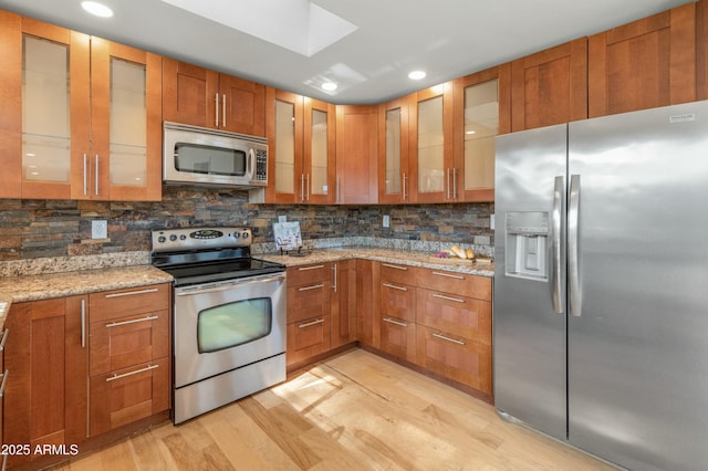 kitchen featuring appliances with stainless steel finishes, light hardwood / wood-style flooring, light stone counters, and tasteful backsplash