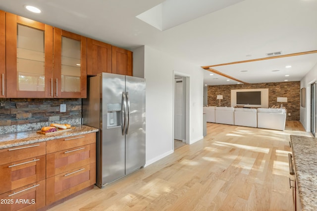 kitchen featuring light stone countertops, light wood-type flooring, backsplash, and stainless steel refrigerator with ice dispenser