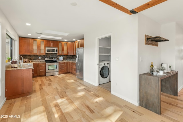 kitchen with washer / clothes dryer, appliances with stainless steel finishes, light wood-type flooring, light stone counters, and decorative backsplash