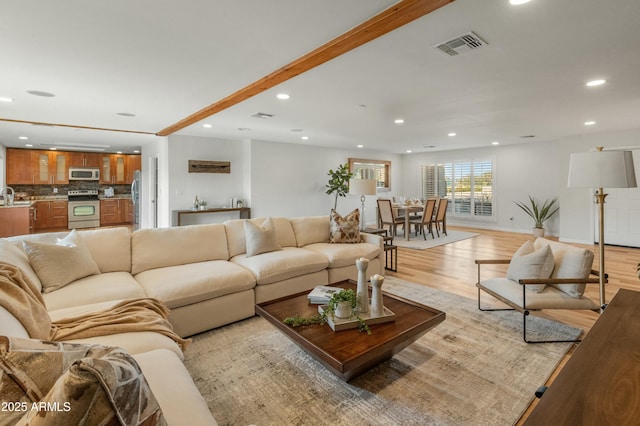 living room featuring sink, light hardwood / wood-style floors, and beam ceiling