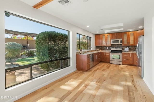 kitchen with stainless steel appliances, sink, light hardwood / wood-style flooring, decorative backsplash, and light stone countertops