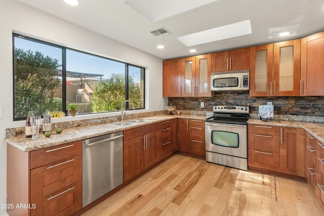 kitchen featuring sink, light hardwood / wood-style floors, a skylight, light stone countertops, and appliances with stainless steel finishes