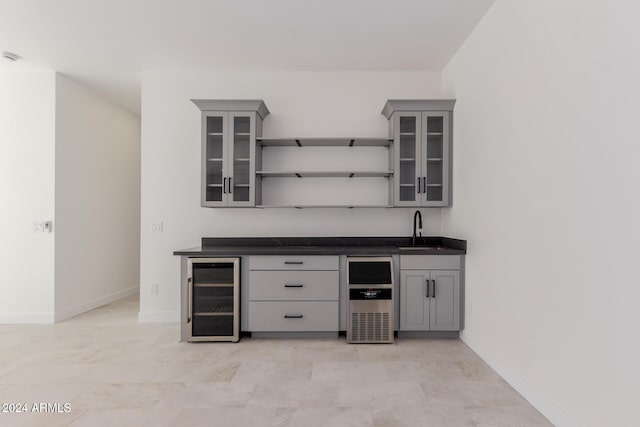 bar featuring beverage cooler, gray cabinetry, and sink