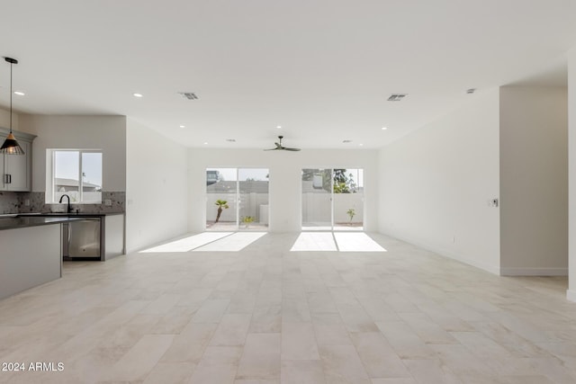 unfurnished living room featuring ceiling fan, sink, and a healthy amount of sunlight