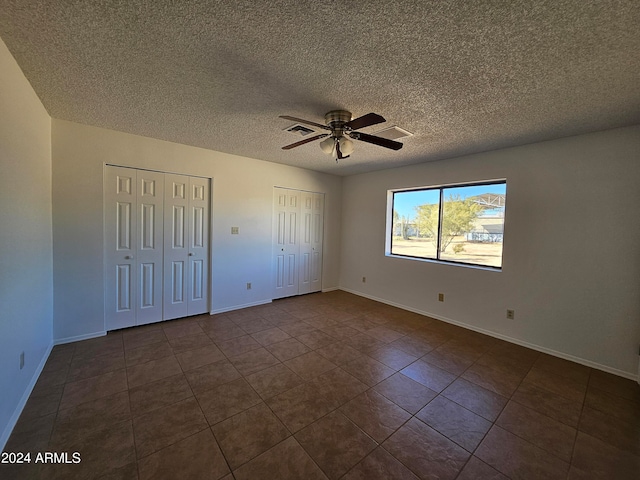 unfurnished bedroom with dark tile floors, ceiling fan, two closets, and a textured ceiling