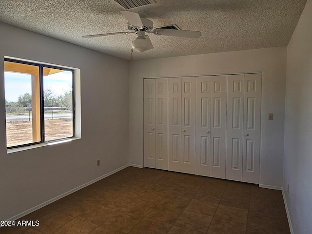 unfurnished bedroom featuring dark tile floors, ceiling fan, a textured ceiling, and a closet