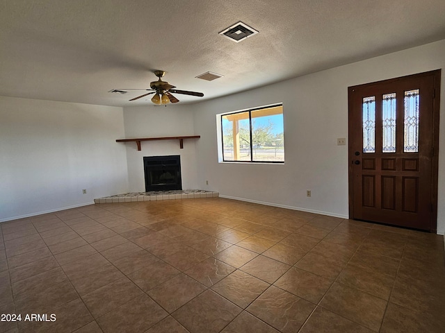 unfurnished living room with a tiled fireplace, ceiling fan, dark tile flooring, and a textured ceiling