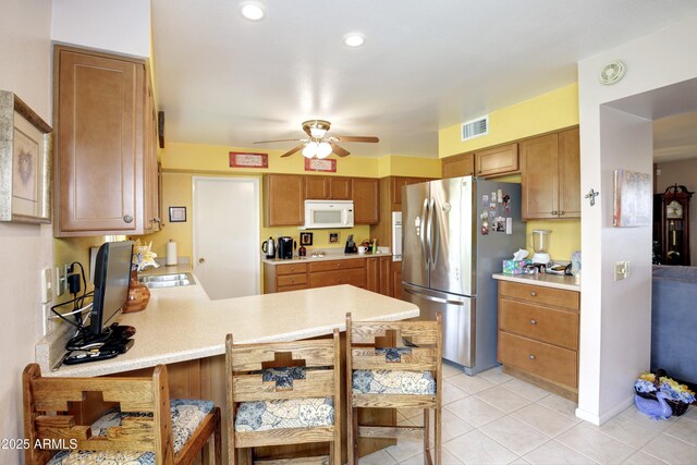 kitchen featuring a peninsula, white microwave, light countertops, and freestanding refrigerator