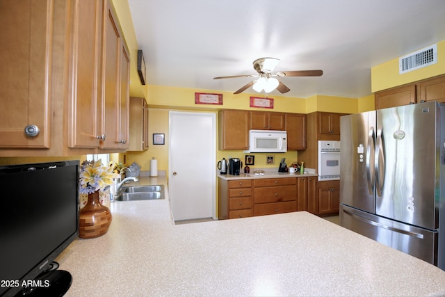 kitchen with light countertops, visible vents, brown cabinetry, a sink, and white appliances