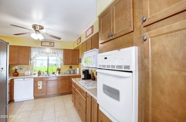 kitchen with brown cabinets, light countertops, a sink, ceiling fan, and white appliances