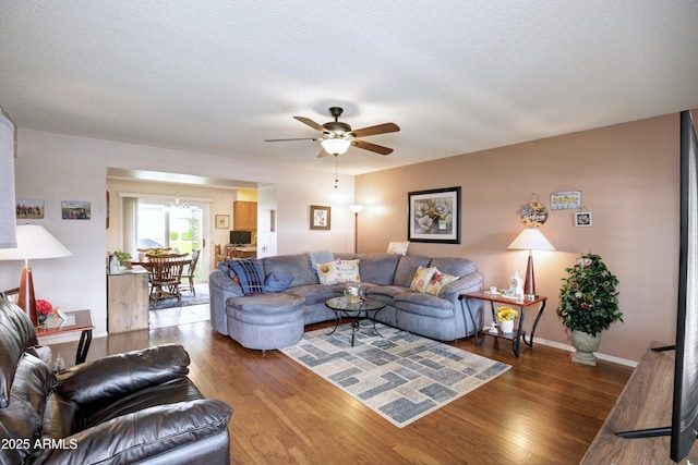 living area with ceiling fan, a textured ceiling, baseboards, and wood finished floors