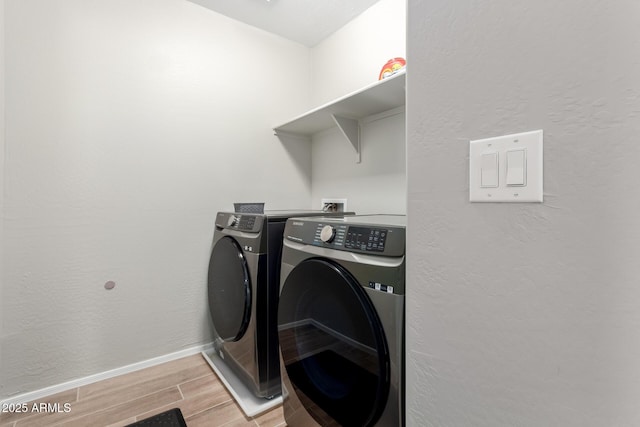 clothes washing area with baseboards, separate washer and dryer, a textured wall, laundry area, and wood finish floors