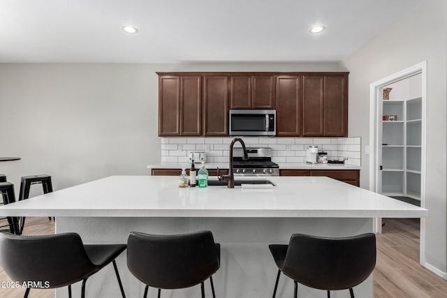 kitchen featuring stainless steel appliances, light wood finished floors, a breakfast bar, and backsplash
