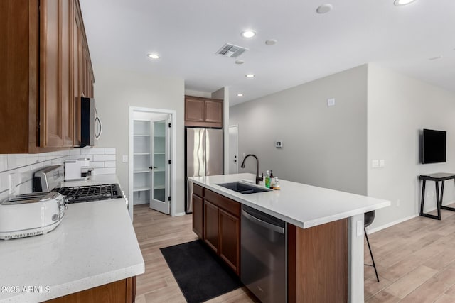 kitchen with tasteful backsplash, light wood-type flooring, visible vents, stainless steel appliances, and a sink