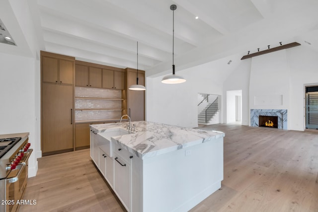 kitchen featuring light wood-type flooring, decorative light fixtures, light stone countertops, high end stove, and white cabinets