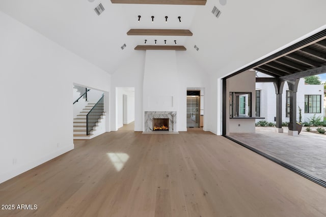 unfurnished living room with high vaulted ceiling, light hardwood / wood-style flooring, a high end fireplace, and beamed ceiling