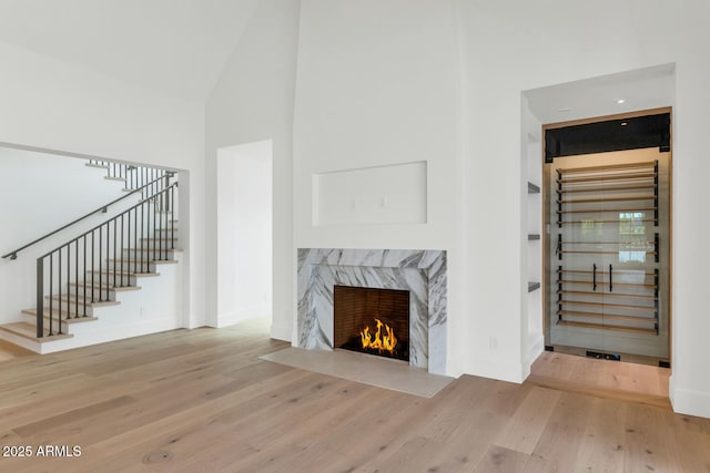 living room with a high end fireplace, light hardwood / wood-style flooring, and high vaulted ceiling