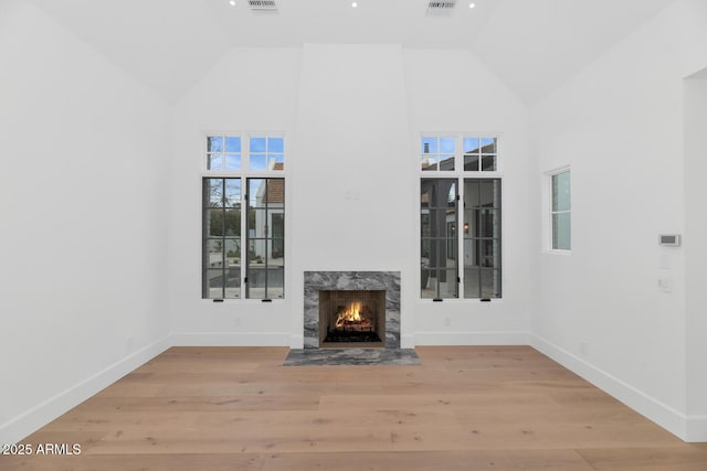 unfurnished living room featuring high vaulted ceiling, light hardwood / wood-style floors, and a high end fireplace