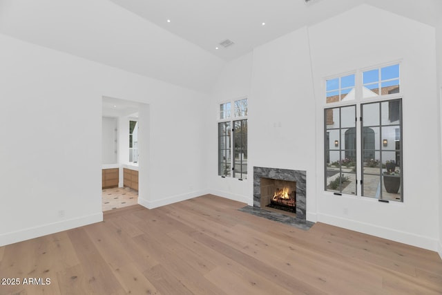 unfurnished living room with a premium fireplace, high vaulted ceiling, light hardwood / wood-style floors, and plenty of natural light