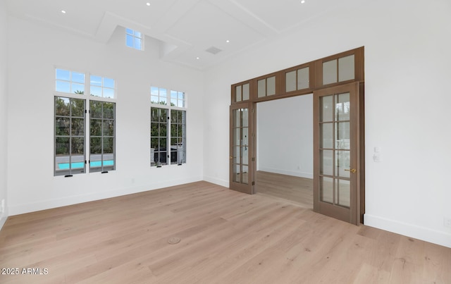 empty room featuring french doors, a towering ceiling, coffered ceiling, beam ceiling, and light hardwood / wood-style floors