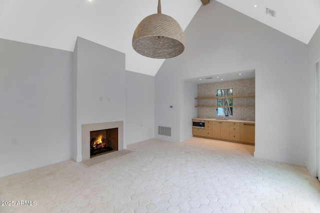 unfurnished living room featuring a high end fireplace, sink, and high vaulted ceiling