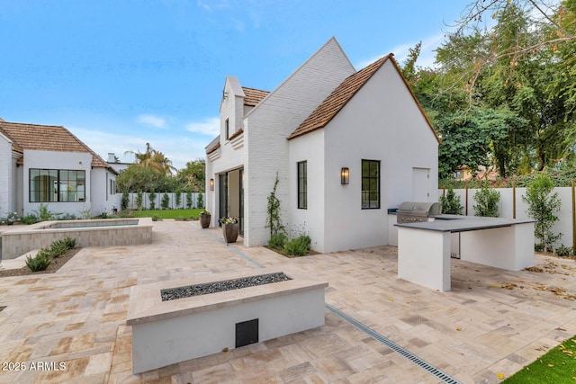 view of patio / terrace with an in ground hot tub, a grill, an outdoor fire pit, and exterior kitchen