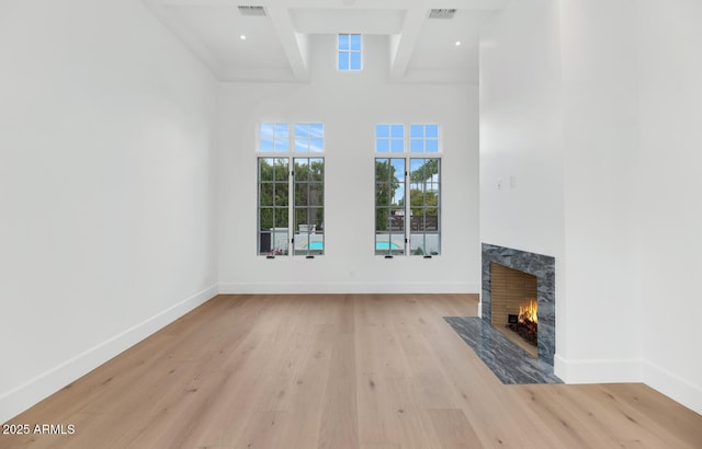 unfurnished living room with beam ceiling, a towering ceiling, light hardwood / wood-style flooring, and a premium fireplace