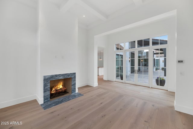 unfurnished living room with beam ceiling, light wood-type flooring, french doors, and a high end fireplace