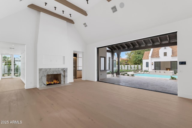 unfurnished living room featuring beam ceiling, high vaulted ceiling, light hardwood / wood-style floors, and a high end fireplace