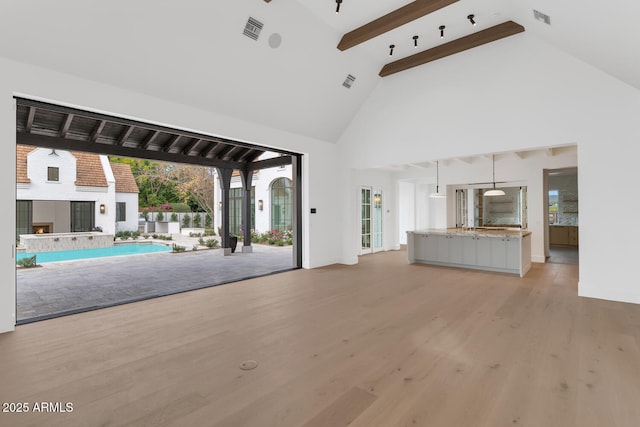 unfurnished living room featuring high vaulted ceiling, light wood-type flooring, and beamed ceiling