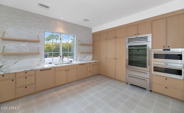 kitchen featuring light brown cabinetry, sink, double oven, and tasteful backsplash