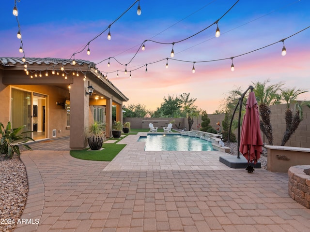 pool at dusk featuring pool water feature and a patio