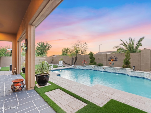 pool at dusk with pool water feature and a patio area