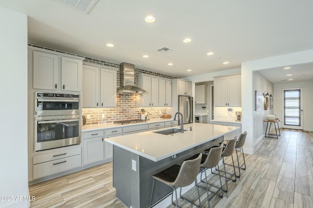 kitchen with a kitchen breakfast bar, stainless steel appliances, wall chimney range hood, sink, and an island with sink