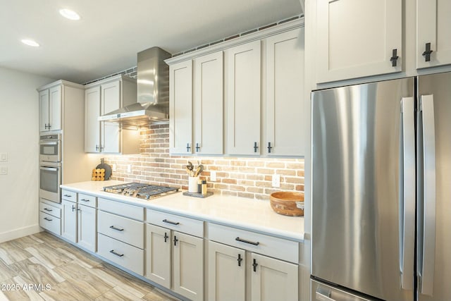 kitchen with white cabinets, wall chimney range hood, light hardwood / wood-style flooring, decorative backsplash, and appliances with stainless steel finishes